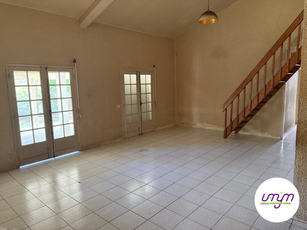 Salon à plafond très haut avec poutre apparente et escalier en bois vers la mezzanine, maison F4 en dur à vendre à Koutio par l’agence Vanym