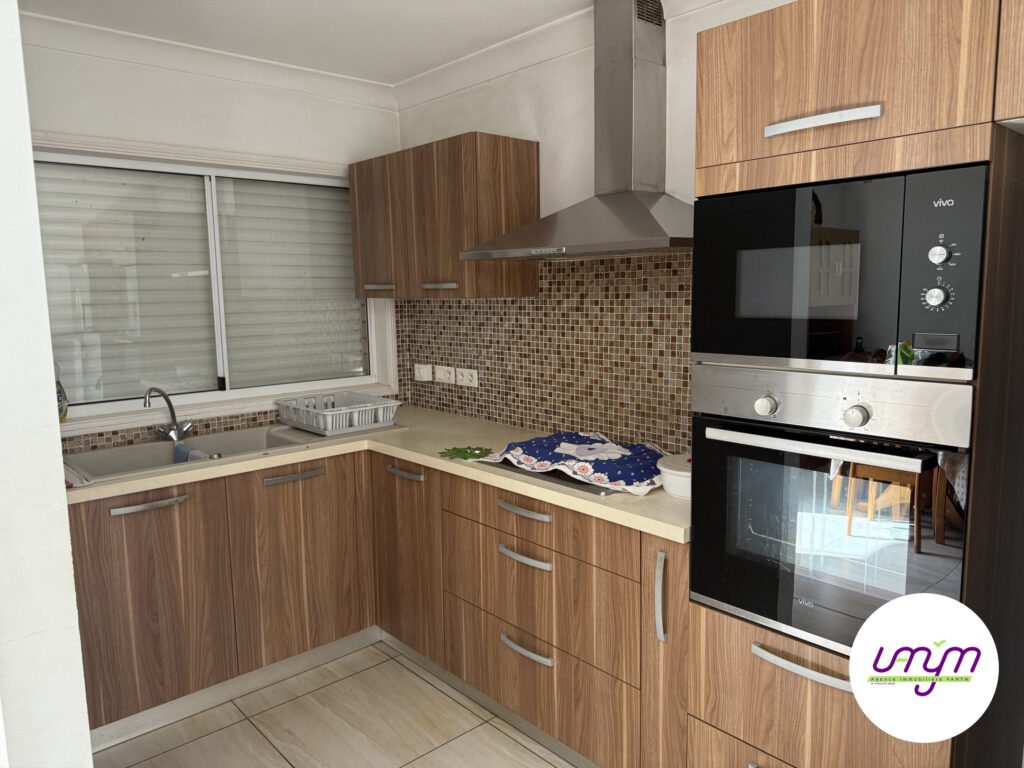 Cuisine équipée en façade bois, avec four et micro-ondes encastrés et hotte.